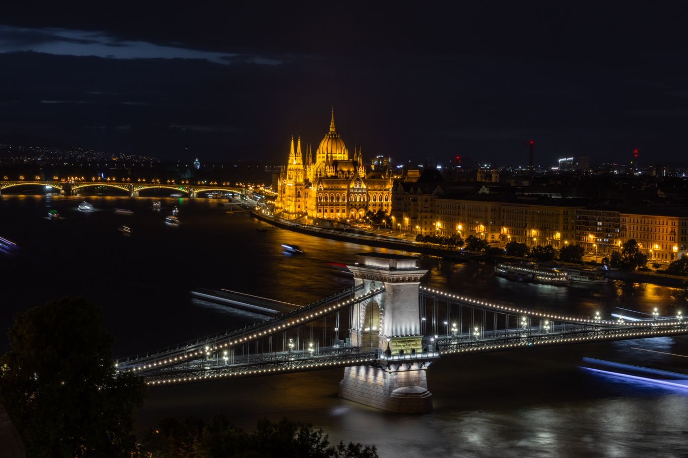 A budapesti Lánchíd és a Parlament esti kivilágításban, a Duna partján.